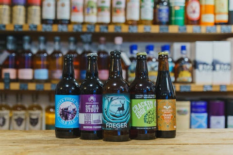 Five beer bottles in front of a shelf with various other bottles
