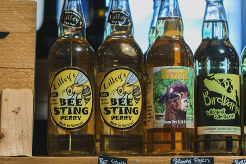 Row of cider and perry bottles on a wooden shelf.