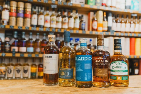 Four bottles of whiskey on a bar counter with a background of shelves filled with various bottles.